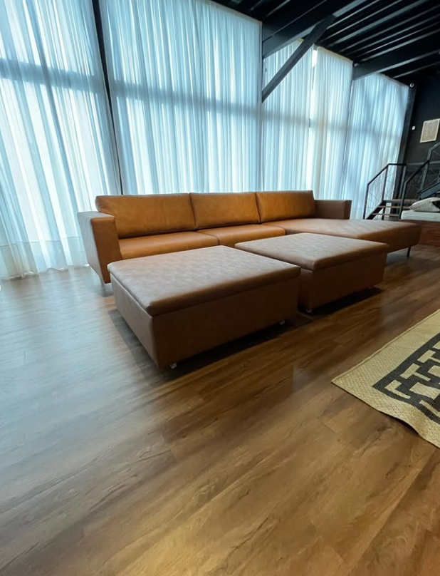 Sofá de couro caramelo com dois puffs em loft de pé-direito alto