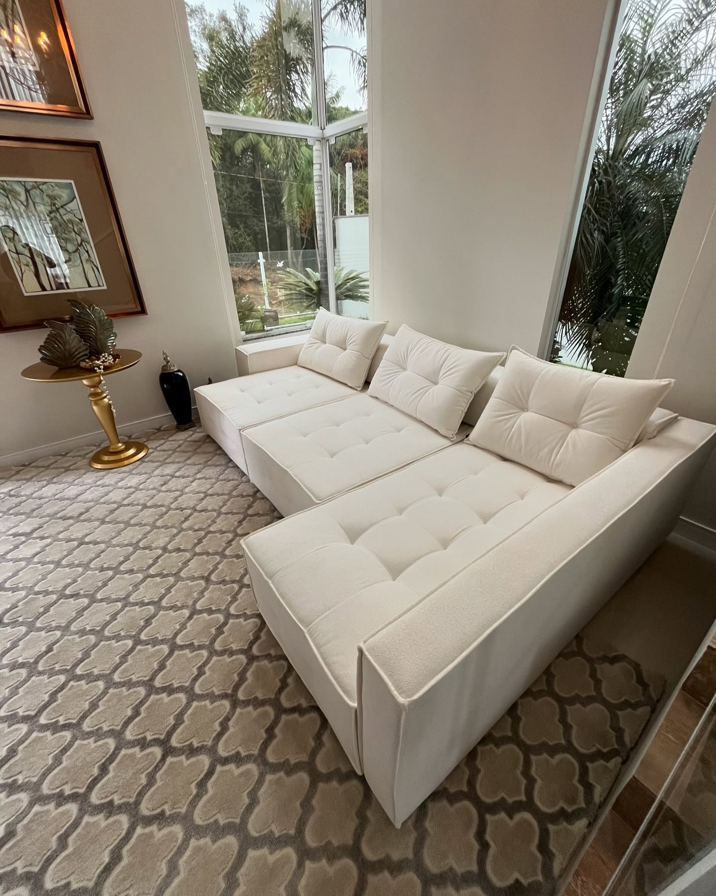 Sofá modular sob medida em tecido off-white com capitonê em sala com janelas amplas