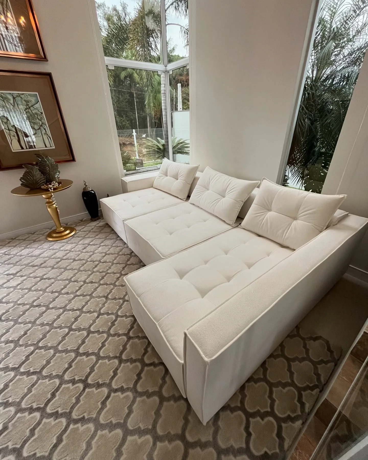 Sofá modular sob medida em tecido off-white com capitonê em sala com janelas amplas